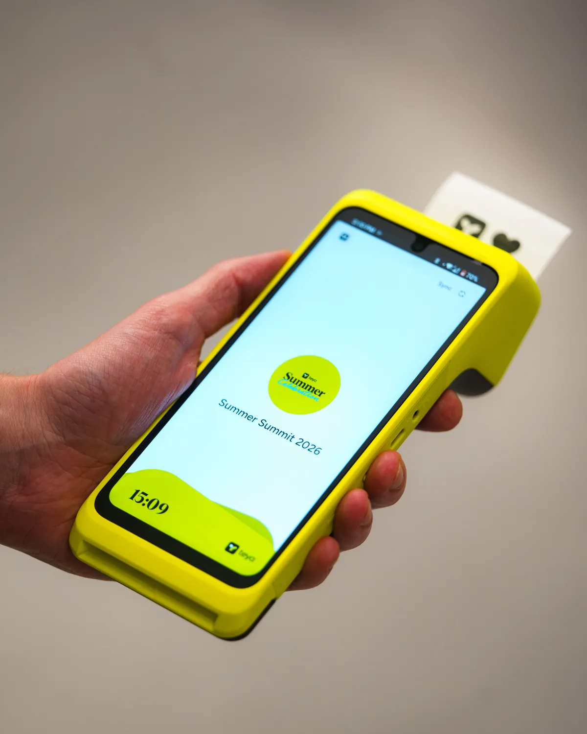A hand holding a Teya Pro with a receipt just printed, the screen showing a Teya summer summit graphic.