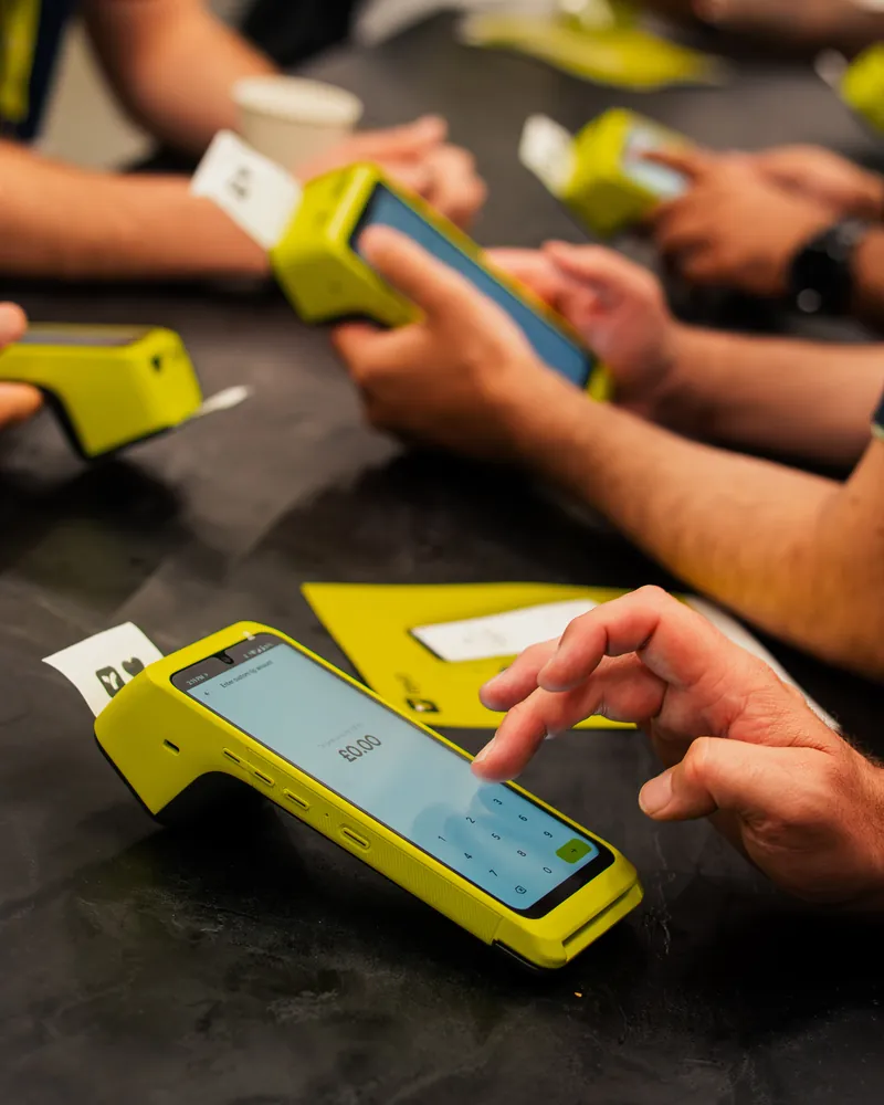 Hands using a Teya Pro at a dark table as a receipt prints, another business trading.